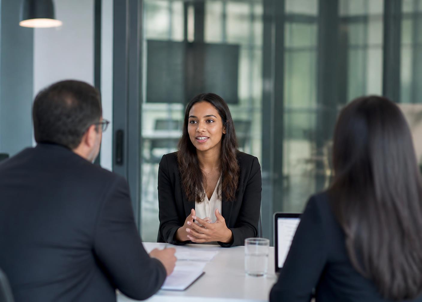 Professional candidate speaking with two interviewers in a modern glass meeting room